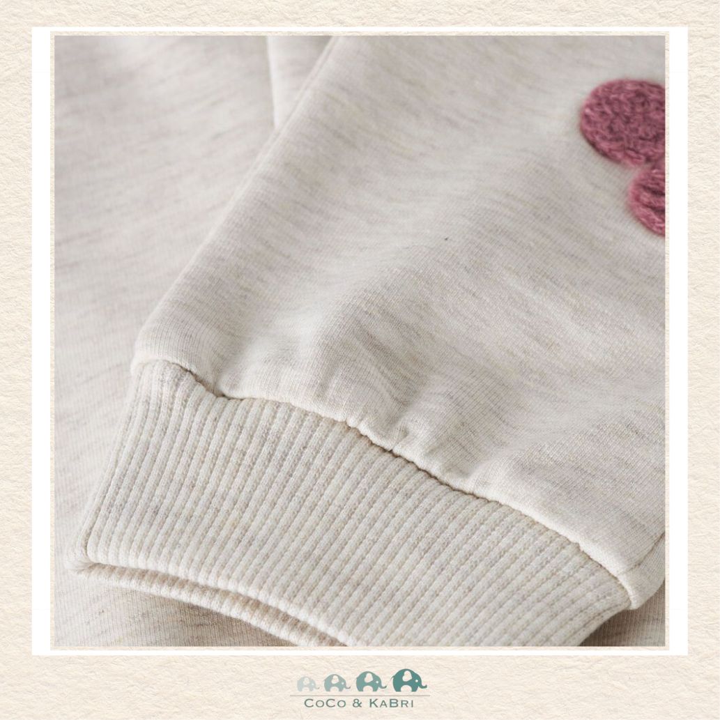 Close-up of a beige sweater with ribbed cuffs and hem, featuring a pink flower design on a light background., Brooks Alberta Canada