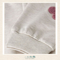 Close-up of a beige sweater with ribbed cuffs and hem, featuring a pink flower design on a light background., Brooks Alberta Canada