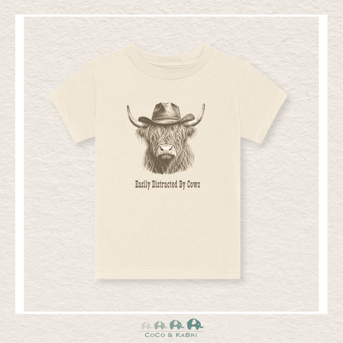 Beige t-shirt with a graphic of a cow wearing a cowboy hat and text 'Easily Distracted By Cows' on a textured beige background.